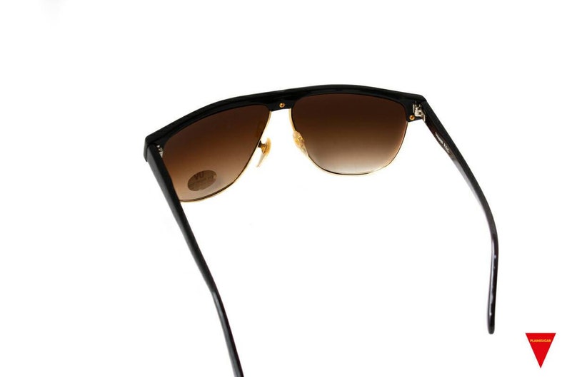 May include: Black sunglasses with brown gradient lenses and gold accents. The sunglasses have a wraparound design and are made of a lightweight material.
