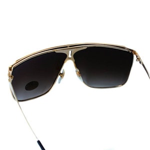 May include: Gold-tone aviator sunglasses with dark brown lenses. The sunglasses have a thin metal frame and are designed with a wraparound style.