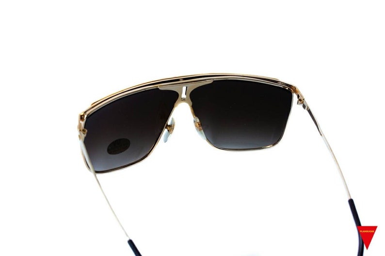 May include: Gold-tone aviator sunglasses with dark brown lenses. The sunglasses have a thin metal frame and are designed with a wraparound style.