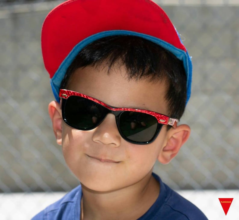 May include: A young person wearing a red and blue baseball cap and red-rimmed sunglasses. The sunglasses have a black lens.