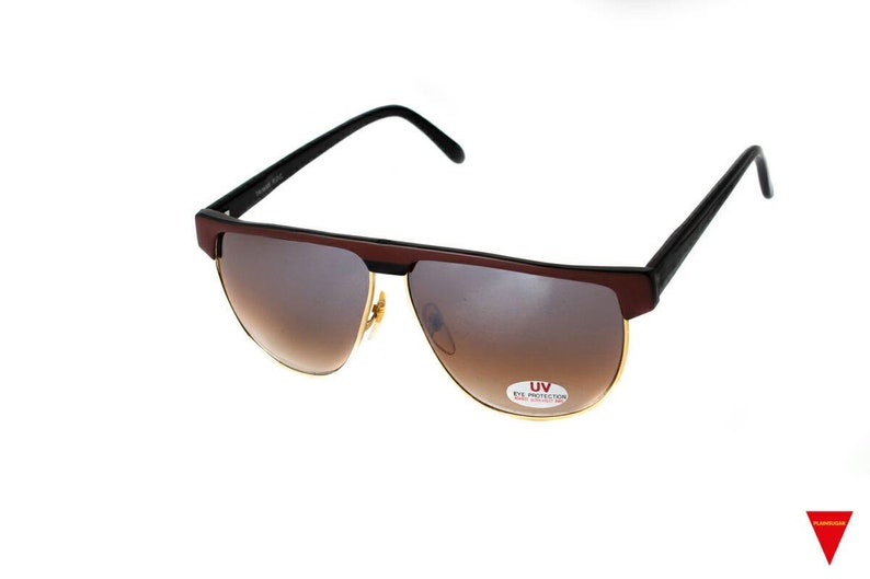 May include: Brown and black sunglasses with gold accents and brown lenses. The sunglasses have a UV eye protection label.