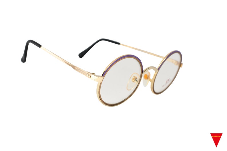 May include: Gold-tone round eyeglasses with purple accents on the rims. The glasses have clear lenses and black plastic temple tips.