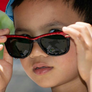 May include: A young person wearing a red and blue baseball cap and sunglasses with red frames. The sunglasses are black and have a reflective lens.