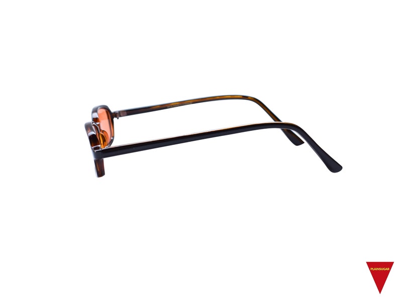 May include: A pair of eyeglasses with a dark brown tortoiseshell frame and orange-tinted lenses. The glasses are shown from a side profile, revealing the thin, curved temples and the rectangular shape of the frames. The design is simple and functional.