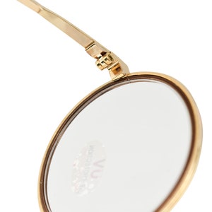 May include: A gold-toned round makeup mirror with a hinged arm. The mirror has a clear glass surface and the text "VU COLLECTION" is printed on the glass.