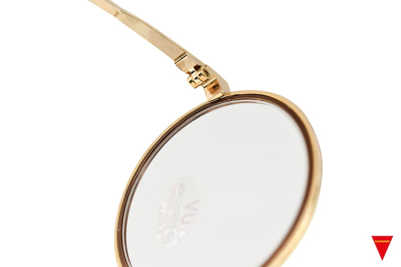 May include: A gold-toned round makeup mirror with a hinged arm. The mirror has a clear glass surface and the text "VU COLLECTION" is printed on the glass.