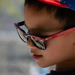 May include: A young person wearing a red and blue baseball cap and black sunglasses with a red frame.