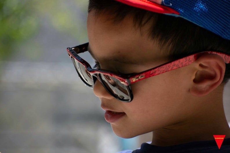 May include: A young person wearing a red and blue baseball cap and black sunglasses with a red frame.