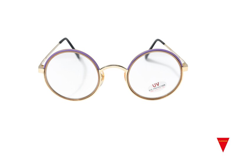 May include: Gold-rimmed round glasses with purple accents and clear lenses. The glasses have a label on the right lens that reads "UV Eye Protection".