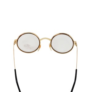 May include: Gold-rimmed round eyeglasses with black temple tips. The glasses have clear lenses.