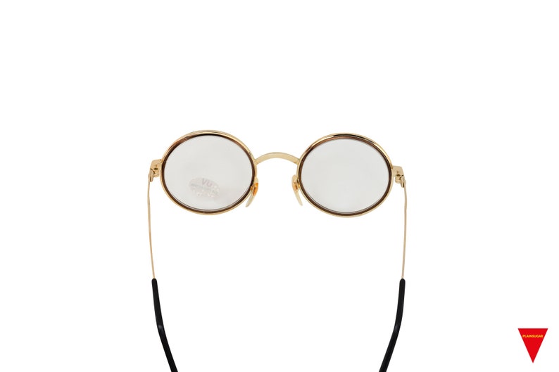 May include: Gold-rimmed round eyeglasses with black temple tips. The glasses have clear lenses.