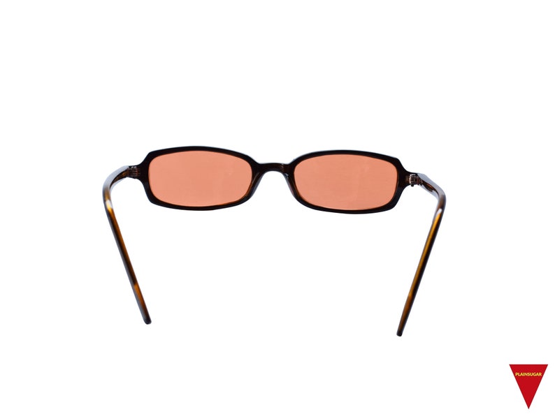 May include: Rectangular sunglasses with a dark brown tortoiseshell frame and light orange tinted lenses. The glasses feature thin, curved temples and a bridge connecting the two oval-shaped lenses. The design is simple with a smooth finish.