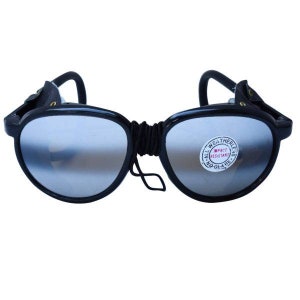 May include: Black safety glasses with a silver mirrored lens and a black elastic strap. The glasses have a label that reads "All Weatherleys, Impact Resistant, Fog-Free".