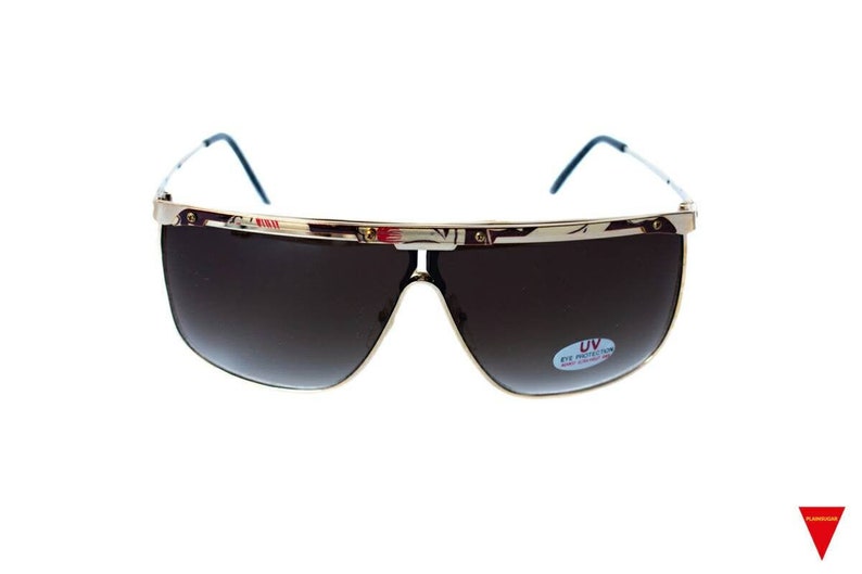 May include: Gold-framed sunglasses with brown lenses. The lenses have a gradient tint and a sticker that says "UV Eye Protection".
