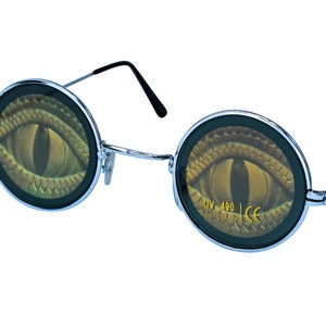 May include: Round sunglasses with a silver frame and black arms. The lenses have a graphic of a green snake eye with gold scales. The text "UV 400 PROTECTED CE" is printed on the right lens.