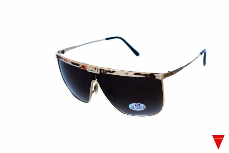 May include: Gold-toned sunglasses with dark lenses and a thin gold frame. The sunglasses have a UV eye protection label on the right lens.