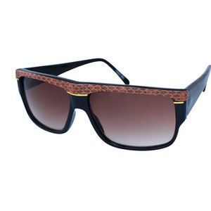Könnte beinhalten: Schwarze Sonnenbrille mit braunen Lederakzenten am Rahmen. Die Gläser sind braun-verlaufend.