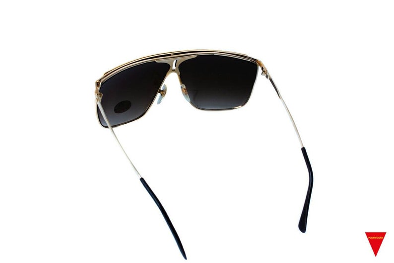 May include: Gold-tone sunglasses with dark brown lenses and black arms. The sunglasses have a square shape and a sleek design.