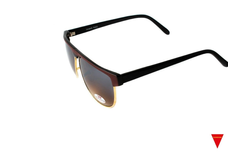 May include: Black sunglasses with brown gradient lenses and a gold trim. The sunglasses have a black frame and a black plastic arm.