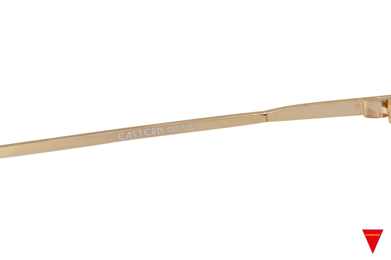 May include: A gold-colored metal frame for eyeglasses with the text "EASTERN OPTICS" printed on the arm.