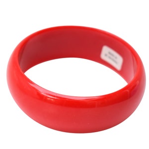 Könnte beinhalten: Ein leuchtend rotes Plastik-Armreif. Das Armband ist glatt und glänzend.