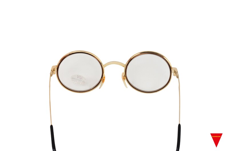 May include: Gold-rimmed round eyeglasses with clear lenses and black temple arms.