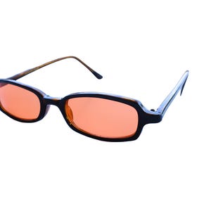 May include: Rectangular sunglasses featuring dark brown tortoise shell frames and vibrant orange tinted lenses. The eyewear has thin, matching brown arms that extend from the sides, providing a clear view of the front and side profile of the glasses.