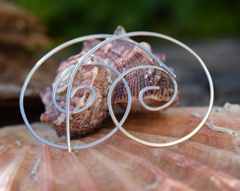 May include: Silver hoop earrings with a spiral design, resting on a seashell.