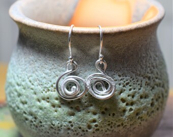 May include: A pair of silver dangle earrings with a spiral design. The earrings are made of a thin, twisted wire that forms a double spiral.