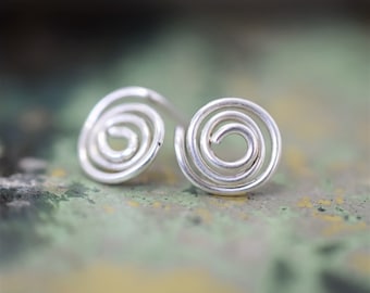May include: A pair of silver spiral stud earrings. The earrings are made of a single piece of wire that is twisted into a spiral shape.