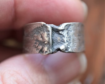 May include: A silver ring with a wide band and a textured surface. The ring is made of two pieces that have been joined together.