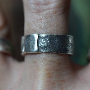 May include: A silver ring with a textured, hammered finish. The ring is wide and flat, and it appears to be handmade.