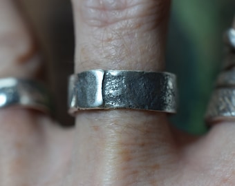 Puede incluir: Un anillo de plata con un acabado texturizado y martillado. El anillo es ancho y plano, y parece estar hecho a mano.