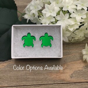 May include: A pair of green turtle earrings in a white box. The box has the text "Color Options Available" printed on the front.