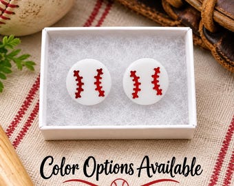 May include: A pair of round white stud earrings featuring a red baseball stitch pattern, presented in a small white box with white padding. The text Color Options Available is printed below the box, accompanied by a small red baseball graphic.