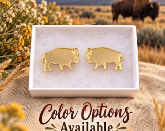 May include: A pair of gold-toned, mirror-finish bison-shaped earrings displayed inside a white box. The earrings are positioned side-by-side on a white foam insert. The text "Color Options Available" is printed in brown below the box.