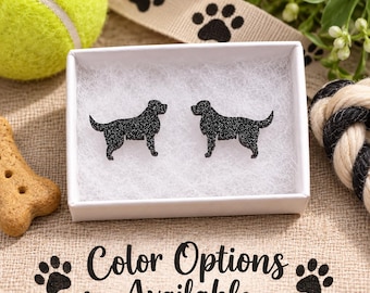 May include: A pair of black glitter dog-shaped stud earrings resting inside a white rectangular gift box filled with white padding. The earrings are shaped like standing dogs in profile. The text Color Options Available is printed below.