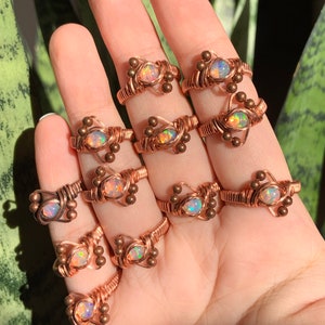 May include: A collection of 10 copper wire wrapped rings with iridescent opal gemstones. Each ring features a unique design with small copper beads.