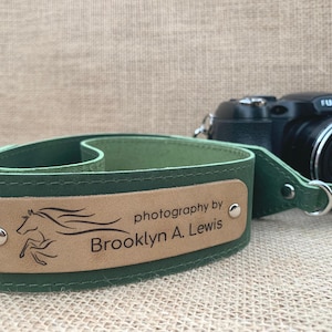 May include: Green leather camera strap with a brown leather patch that says "photography by Brooklyn A. Lewis" and a stylized image of a horse running.