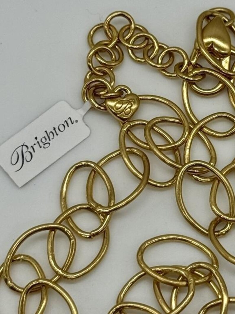 May include: A gold-toned chain necklace with a heart-shaped charm that says "Brighton." The chain is made of interlocking oval links.