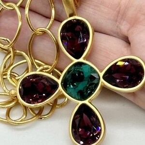 May include: A gold chain necklace with a pendant featuring a four-leaf clover design. The clover is made of four teardrop-shaped stones, two purple and two green.