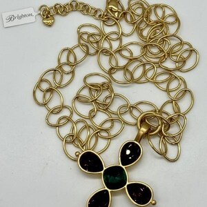 May include: Gold chain necklace with a pendant in the shape of a cross. The cross is adorned with five stones, four purple and one green.