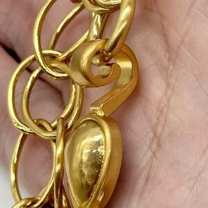 May include: Gold-toned chain with a large, ornate, flower-shaped charm. The chain is made of interlocking circles and has a hook clasp.