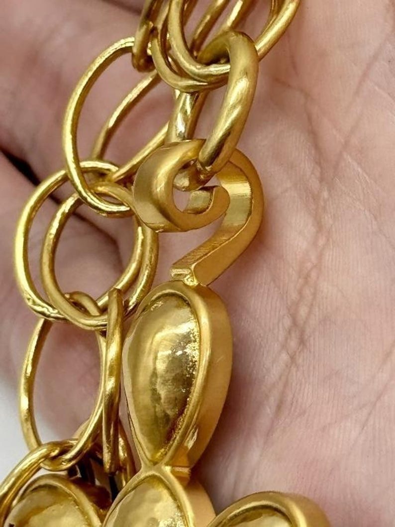 May include: Gold-toned chain with a large, ornate, flower-shaped charm. The chain is made of interlocking circles and has a hook clasp.