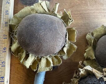May include: Two brown fabric sunflowers with a rustic wooden stem. The sunflowers have a brown centre and green fabric petals.