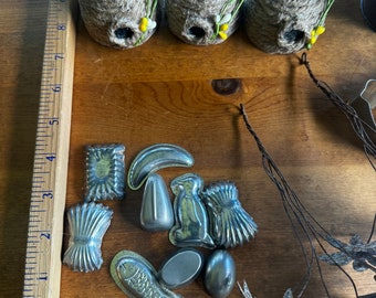 May include: Three small, brown, woven beehive-shaped ornaments with yellow and white flower accents.  A collection of 10 small, silver, metal moulds in various shapes, including a fish, a banana, a rabbit, and a pear.