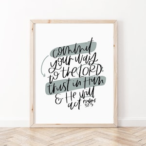 May include: A framed print with a white background and a black and grey quote that reads "Commit your way to the Lord, trust in Him & He will act." The quote is written in a handwritten style with a grey background behind the words. The quote is from Psalms 37:5.