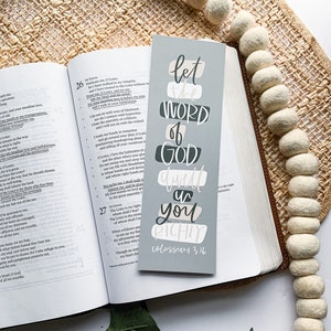 May include: A gray and white bookmark with the text "Let the Word of God dwell in you richly Colossians 3:16". The bookmark has a decorative design with a gray background and white lettering.