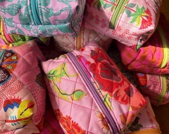 May include: A collection of pink quilted zippered pouches with floral patterns. The pouches are made of fabric and have a quilted texture. The pouches are in various sizes and have different floral designs.