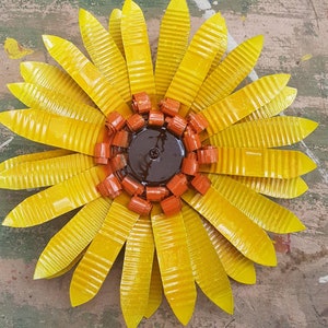 May include: A yellow metal sunflower with a brown center and orange petals. The sunflower is made of recycled materials and has a rustic, handmade look.